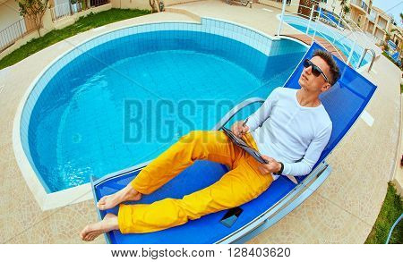 young man relaxing on the chaise-longue near the pool