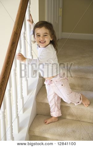 Criança menina caucasiano permanente carpete escadas segurando no corrimão.