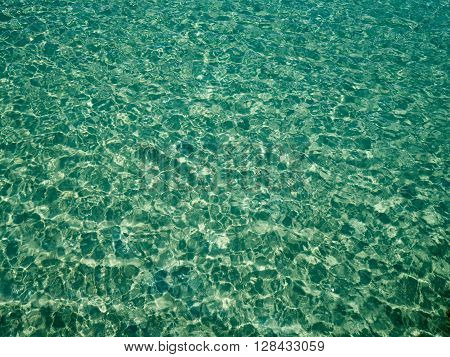 Unique perspective green crystal sea water surface ripple with sun reflection. Water background. Ocean water texture.