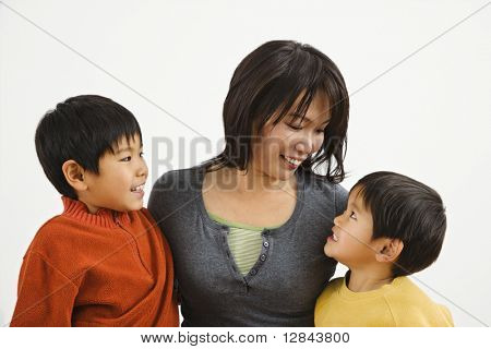 Asiatische Mutter und zwei Söhne, die lächelnd auf einander.