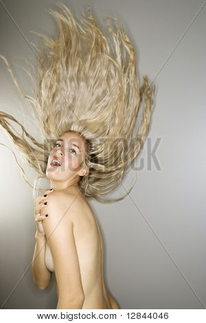Sensuale donna caucasica nuda con bocca aperta lanciando lunghi biondi capelli in aria.
