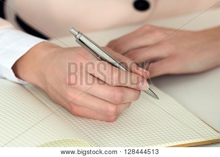 Woman hand holding silver pen ready to make note in opened notebook. Businesswoman or employee at workplace writing business ideas plans tasks at personal organizer. Office life or education concept