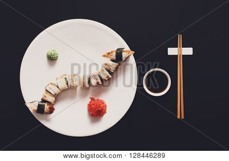 Japanese food restaurant, unagi sushi and roll plate set. One portion. Sushi unagi, chopsticks, ginger and wasabi. Sushi at white round plate, black background. Top view, soy sauce.