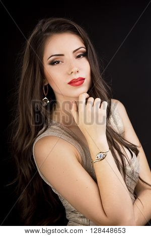Young brunette woman in evening dress with beautiful make-up posing on black background. Looking at camera