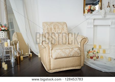 Elegant soft cream arm-chair near a fireplace. Luxury interior in white colors