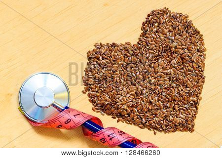 Diet healthcare weight reduction concept. Flax seeds linseed heart shaped stethoscope and measuring tape. Healthy food for preventing heart diseases overweight.