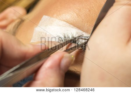 Eyelash extension procedure in beauty salon. Tweezers in hands of tehnician