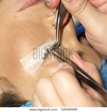 Eyelash extension procedure in beauty salon. Tweezers in hands of tehnician