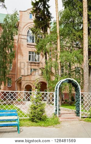 Four-storey building made of red bricks behind the white latticed fence.