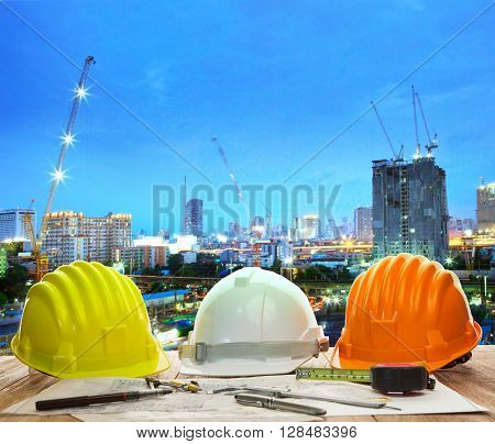 Engineer Working Table With Hard Hat Plan And Writing Tool Against Beautiful Lighting And Urban Buil