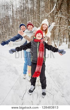 Happy family of four stands on skates on ice pathway in winter park spreading arms to sides.