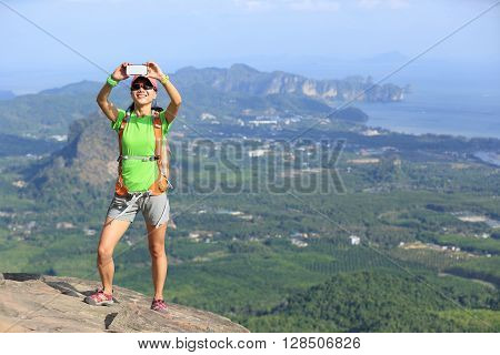 young woman hiker use smartphone taking photo on seaside mountain top
