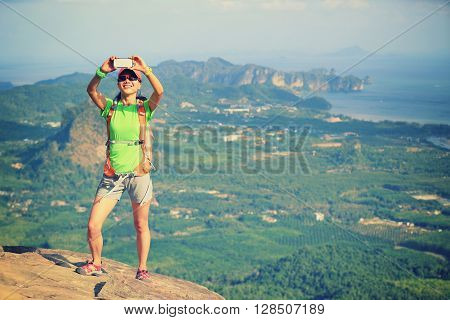 young woman hiker use smartphone taking photo on seaside mountain top