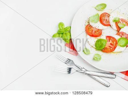 CLassic Italian Caprese salad with tomatoes, mozzarella di Buffala and fresh basil on red and white checkered napkin over white wooden background. Top view, copy space