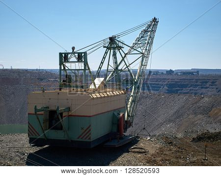 Dragline works at small open cast iron mine filled by water with industrial buildings in the background