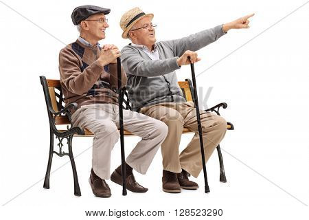 Cheerful senior gentleman showing something to an old friend seated on a bench isolated on white background