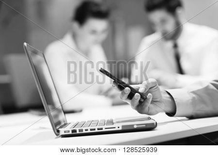close up of  businessman hands  using smart phone and laptop computer, people group in office meeting  room blurred in backgronud