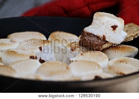 Graham cracker dipping Smores marshmallow dip that has been baked in a cast iron pan. Extreme shallow depth of field and selective focus on marshmallow and chocolate at the end of a graham cracker.