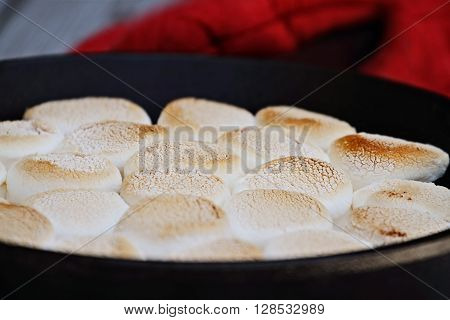 Smores dip baked in a cast iron pan with extreme shallow depth of field and selective focus on center marshmallows.