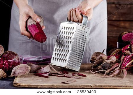 Cook in gray apron is preparing to grate a beetroot with vegetable rasper