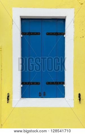 Picturesque old window with blue shutters on light yellow wall (Burano island Venice Italy)