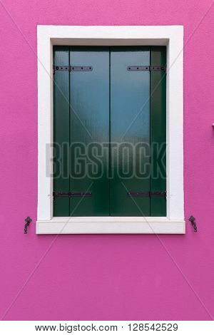 Picturesque old window with dark green shutters on pink (fucsia) wall (Burano island Venice Italy)