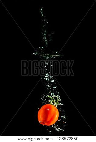 tomato on the black background falling on the water