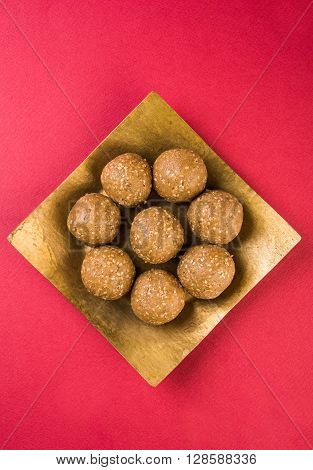 The indian sesame sweet or tilgul laddu, made up of jaggery and sesame seeds, hand made, round, indian sweet prepared in Makar Sankranti festival, served in a square brass plate, top and isolated
