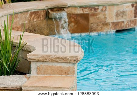 Beautiful swimming pool with flagstone wall that has waterfall pouring out of it.