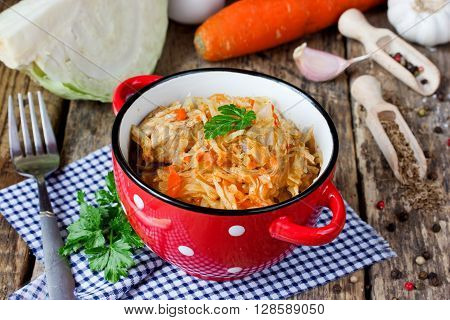 Stewed cabbage with meat vegetables and spices on wooden table with ingredients selective focus