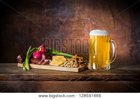 mug of unfiltered beer with sausage, onion, radish, cheese, nuts, toast on cutting board