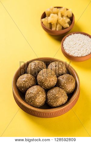 The indian sesame sweet or tilgul laddu or til gul laddu, made up of jaggery and sesame seeds, indian sweet for Makar Sankranti festival, in terracotta bowl with jaggery & raw sesame, isolated on white background
