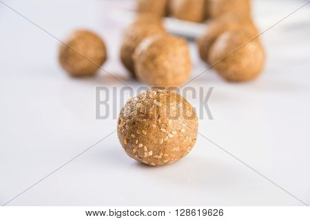 tilgul or til gul laddu, isolated on white background, showing wooden plate full of laddu in background, selective focus