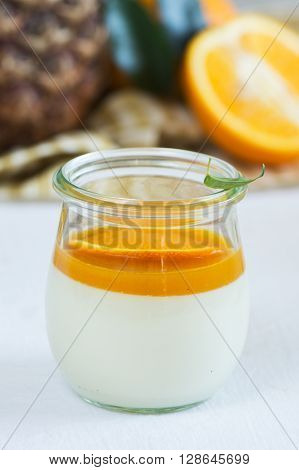 Portion of vanilla panna cotta with exotic fruits sauce in a glass jar over white wooden table. Selective focus