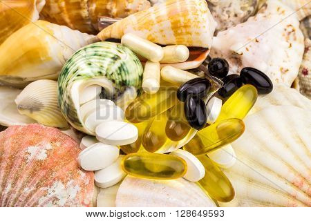 Mixed natural food supplement pills on the beautiful seashells background omega 3 calcium carotene glucosamine capsules
