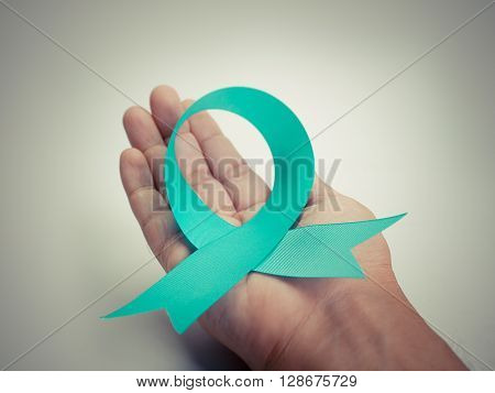 Blue Ribbon In human hands On a white background to support Ovarian Cancer . (Vintage Image)