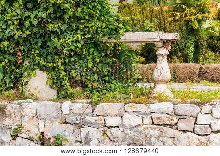 Dilapidated stone fortress wall with bushes in the old park close-up