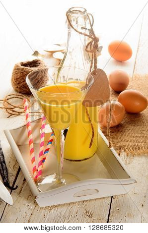 egg liqueur in a cocktail glass and a glass bottle eggs vanilla beans straw on serving tray