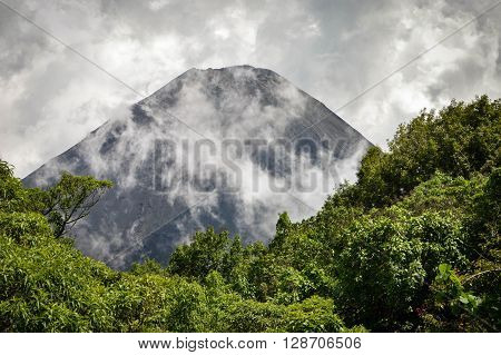 The perfect peak of the active and young Izalco volcano seen from a view point in Cerro Verde National Park in El Salvador covered with thick white clouds