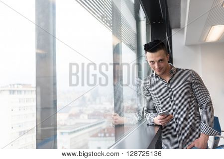 relaxed young businessman using smart phone at modern startup business office meeting room  with big window and city in backgronud