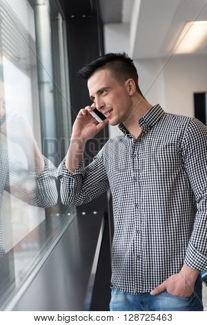 relaxed young businessman speaking on smart phone at modern startup business office meeting room  with big window and city in backgronud