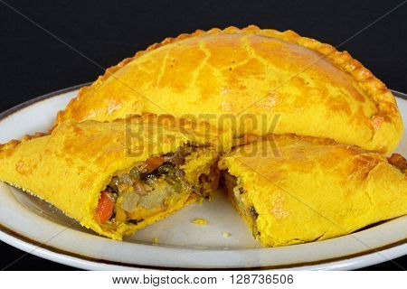 Vegetarian pasty cut in half filled with cheddar cheese onion carrot swede potato and sweet potato in an all butter pastry flavoured with turmeric.