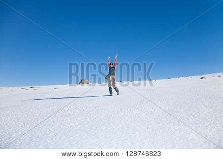 brunette sport active woman with green red and brown clothes hiking looking and arms up gesturing victory in snow with blue sky in Gredos mountain Avila Spain Europe