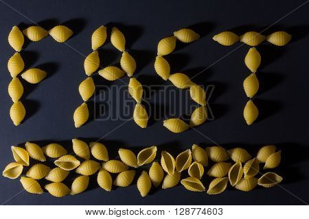 word pasta laid out in the form of seashells on a dark background . FAST/
