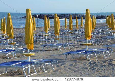 Closed Sun Umbrellas On Sea Beach With Sun Loungers And Deckchairs