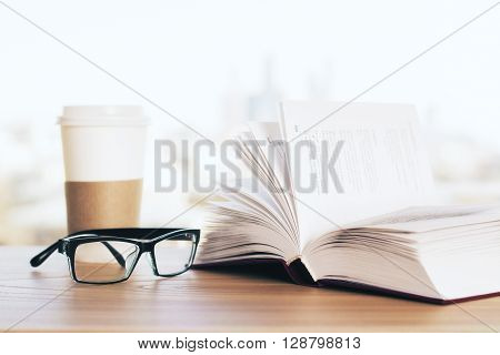 Open book glasses and coffee on wooden desk and blurry background