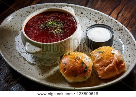 red borscht with sour cream, wild garlic, bread on a wooden background, rustic