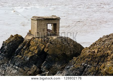 Abandoned defence post on British coast. A concrete gun station stands on rocks on the shore of the Bristol Channel, in Somerset, UK, part of an historic fort used in World War 2