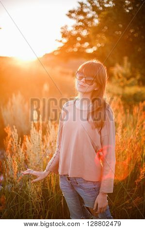 Portrait of young modern girl on the background of nature. Young woman  on a background sunset. Young woman in ripped jeans. in sun glasses
