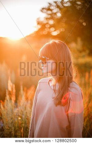 Portrait of young modern girl on the background of nature. Young woman  on a background sunset. Young woman in ripped jeans. in sun glasses
